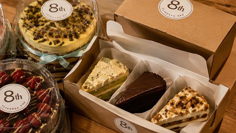 Packaged whole cakes and a box of cake slices with 8th Espresso Bar stickers, ready for pickup